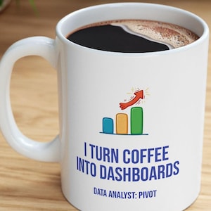 May include: A white ceramic mug filled with black coffee. The front features a colorful bar chart graphic with an upward-pointing red arrow and the blue text: I TURN COFFEE INTO DASHBOARDS. Below this, the text reads: DATA ANALYST: PIVOT.
