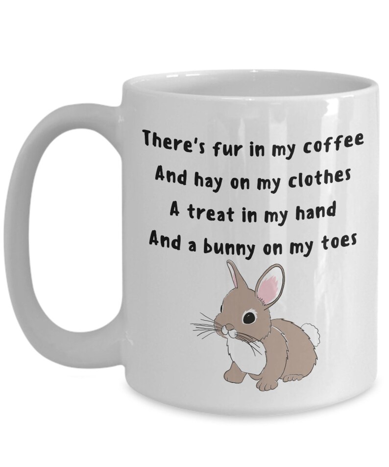 May include: White ceramic mug with a handle. The mug has the text "There's fur in my coffee, And hay on my clothes, A treat in my hand, And a bunny on my toes." A cartoon bunny illustration is also on the mug.