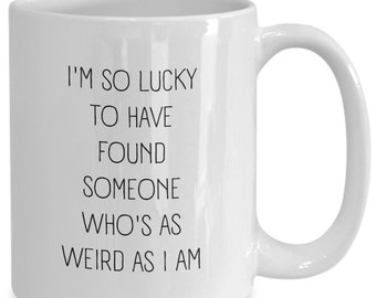 May include: White ceramic mug with a curved handle. The mug features black text that reads, "I'M SO LUCKY TO HAVE FOUND SOMEONE WHO'S AS WEIRD AS I AM."