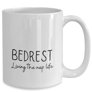 May include: White ceramic coffee mug with black text that reads "Bedrest Living the nap life".