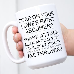 May include: White ceramic coffee mug with black text that reads "Scar on your lower right abdomen? Shark attack, alien apocalypse, top secret mission, particularly intense game of twister, axe throwing."