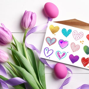Può includere: Una natura morta con un bouquet di tulipani viola, un nastro decorativo e una carta con illustrazioni di cuori colorati. Sono presenti anche due uova di Pasqua rosa, che creano una composizione festosa e artistica.