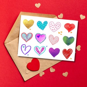 Può includere: Un biglietto di auguri con dodici illustrazioni di cuori colorati in vari stili, tra cui oro ed effetti acquerello. Il biglietto è all'interno di una busta marrone, con un cuore rosso e piccoli ritagli di cuore sparsi su uno sfondo rosso.