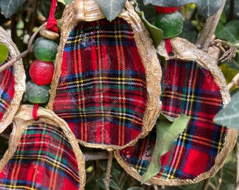May include: Handmade oyster shell ornaments with a red, green, and yellow plaid fabric interior. The shells have a gold-colored trim and are strung with red cord and colorful beads. These unique ornaments are perfect for holiday decor.