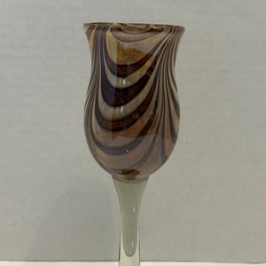 Può includere: Un calice da vino in vetro a strisce marroni e bianche, con gambo trasparente e base viola iridescente.