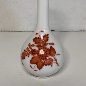 May include: A small white porcelain vase with a brown floral design and gold trim. The vase has a round body and a long, thin neck.