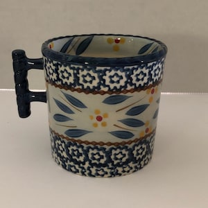 May include: A blue and white ceramic mug with a floral pattern and a blue handle. The mug has a white interior.