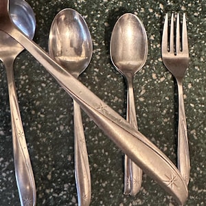 May include: A set of four silver-plated utensils, including a ladle, two spoons, and a fork. The utensils have a starburst design on the handles.
