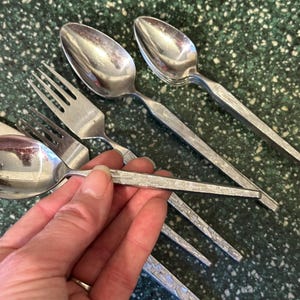 May include: A set of silver cutlery with textured handles. The set includes spoons and forks.