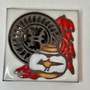 May include: A ceramic tile with a black and white design of a stylized bird in a pot with red and gold accents. The tile has a white background.