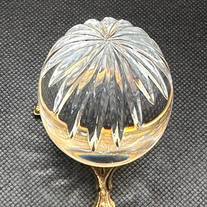 May include: A clear, cut-glass bowl with a gold-colored rim and base. The bowl has a starburst pattern on the top and is supported by a decorative, gold-colored foot. The bowl is likely a decorative item.