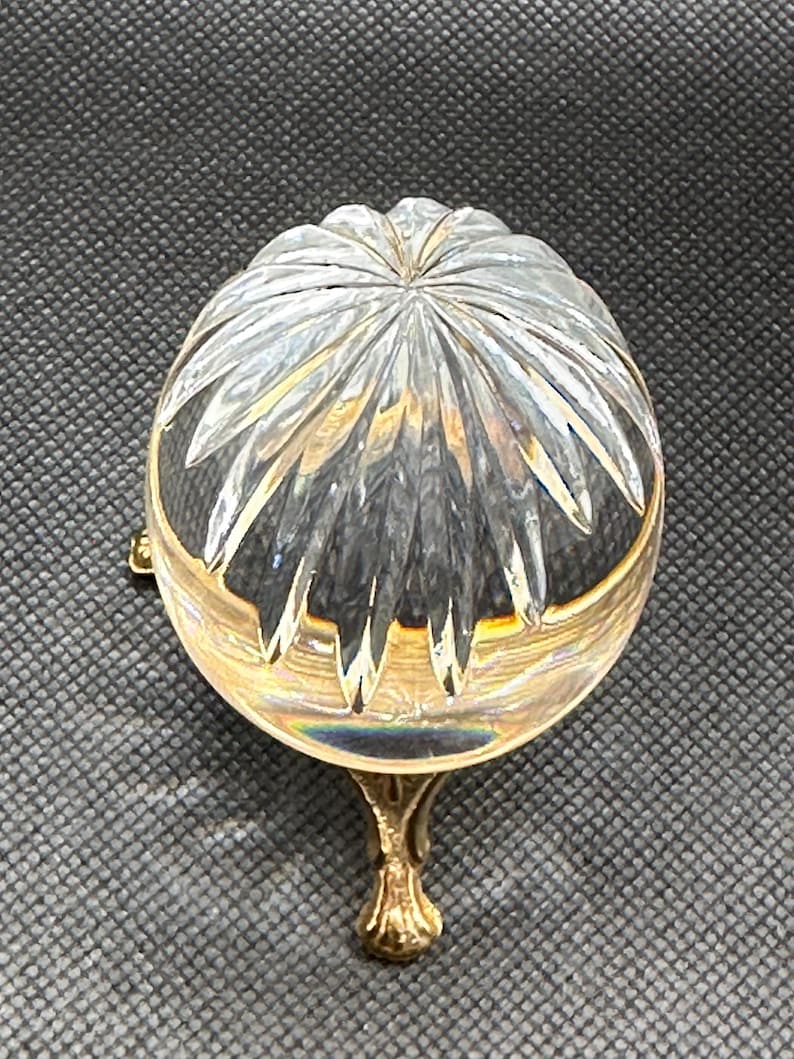 May include: A clear, cut-glass bowl with a gold-colored rim and base. The bowl has a starburst pattern on the top and is supported by a decorative, gold-colored foot. The bowl is likely a decorative item.