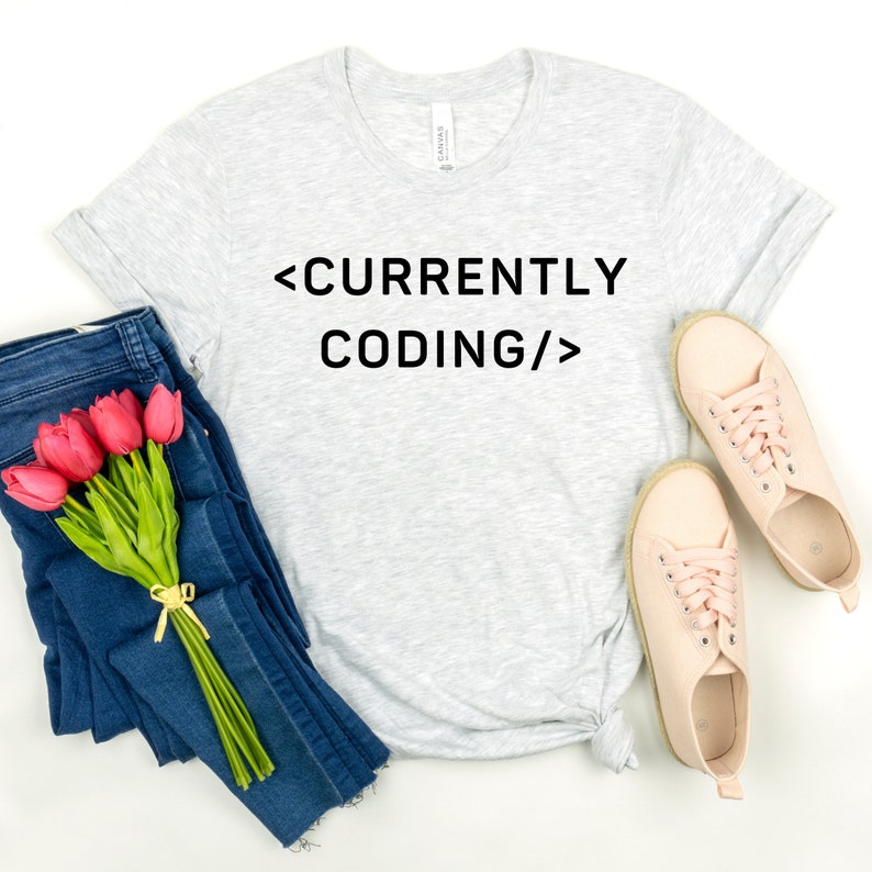 Op de afbeelding: Een grijs t-shirt met de tekst "<CURRENTLY CODING/>" in zwart gedrukt.