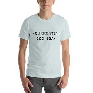 Op de afbeelding: Een lichtblauw t-shirt met de tekst "<CURRENTLY CODING/>" in zwart.