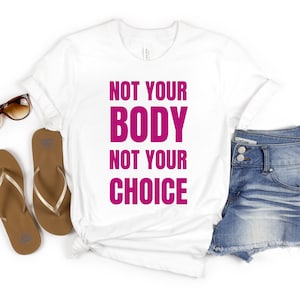 Peut inclure: T-shirt blanc avec le texte "Not Your Body Not Your Choice" imprimé en rose.