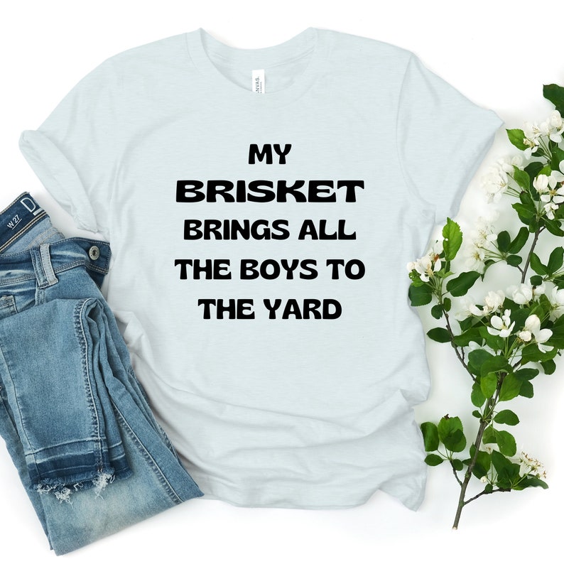 May include: A light blue t-shirt with black text that reads "My Brisket Brings All The Boys To The Yard".