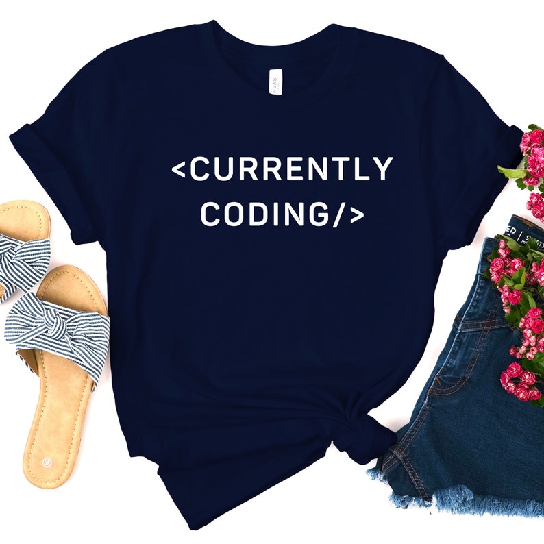 Op de afbeelding: Een donkerblauw t-shirt met witte tekst die "<CURRENTLY CODING/>" zegt.