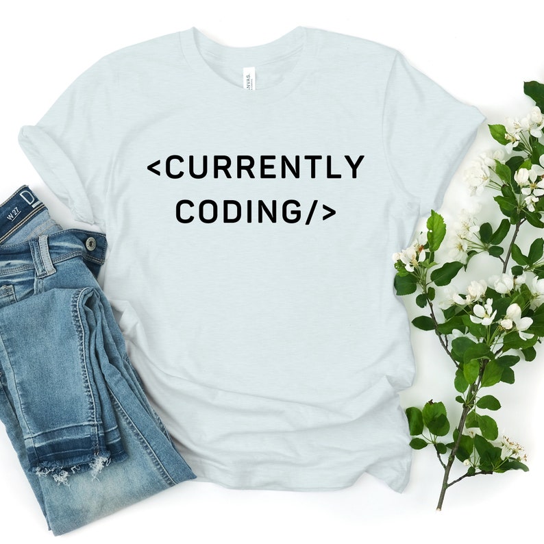 Op de afbeelding: Een lichtblauw t-shirt met de tekst "<CURRENTLY CODING/>" in zwart.