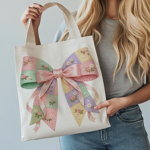 May include: Cream-colored tote bag featuring a large, pastel-colored bow design. The bow is made of patchwork squares in shades of pink, green, purple, and yellow, adorned with floral accents. A pink satin ribbon adds a delicate touch to this charming accessory.