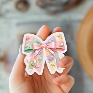 May include: A pastel-colored sticker in the shape of a bow. The bow features a patchwork design with pink, green, and purple squares, adorned with small floral accents. A pink satin ribbon is tied in the center, adding a delicate touch.