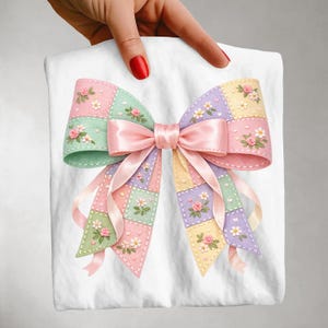 May include: A pastel-colored bow with a patchwork design, featuring squares of pink, green, yellow, and purple. The bow is adorned with embroidered flowers and a pink satin ribbon. The bow is held against a white background.