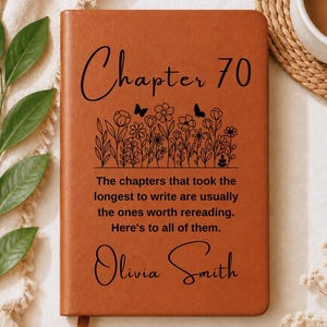 May include: A tan leather-bound journal featuring the black text Chapter 70, a line drawing of wildflowers and butterflies, and the quote: The chapters that took the longest to write are usually the ones worth rereading. Here's to all of them. Olivia Smith.