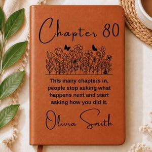 May include: A tan leather-bound journal featuring the black text Chapter 80, a floral and butterfly illustration, and the quote This many chapters in, people stop asking what happens next and start asking how you did it, personalized with Olivia Smith.
