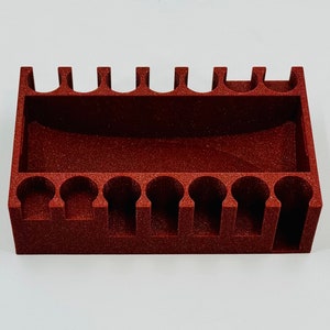 May include: A red plastic organiser with 12 compartments for holding small items. The organiser has a textured surface and is designed to hold items upright.