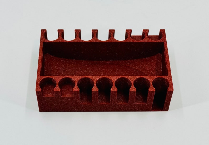 May include: A red plastic organiser with 12 compartments for holding small items. The organiser has a textured surface and is designed to hold items upright.
