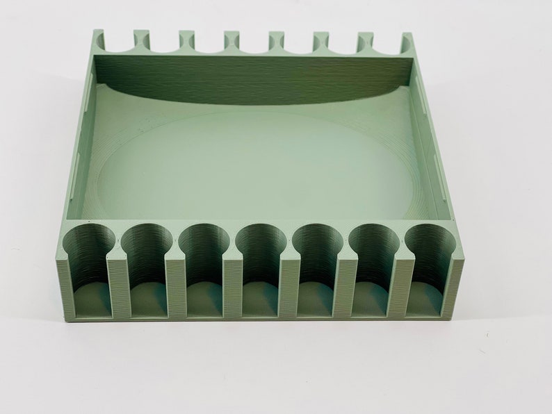 Op de afbeelding: Een saliegroene, rechthoekige organizer met een reeks cilindrische sleuven langs &eacute;&eacute;n kant en een groter, open compartiment. De bovenrand heeft een reeks kleine, rechthoekige uitsteeksels. Het item is gemaakt van een effen, matte materiaal.