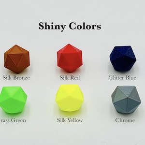 May include: A collection of ten geometric dice in various colours, including glitter red, silk bronze, silk red, glitter blue, silk blue/purple, glitter green, grass green, silk yellow, chrome, and yellow gold. The dice are arranged in two rows of five, with the text "Shiny Colors" at the top of the image.