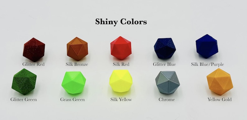 May include: A collection of ten geometric dice in various colours, including glitter red, silk bronze, silk red, glitter blue, silk blue/purple, glitter green, grass green, silk yellow, chrome, and yellow gold. The dice are arranged in two rows of five, with the text "Shiny Colors" at the top of the image.