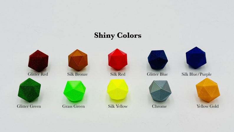 Op de afbeelding: Een verzameling van tien veelkleurige dobbelstenen in glanzende kleuren, waaronder Glitter Red, Silk Bronze, Silk Red, Glitter Blue, Silk Blue/Purple, Glitter Green, Grass Green, Silk Yellow, Chrome en Yellow Gold. De tekst "Shiny Colors" is zichtbaar.