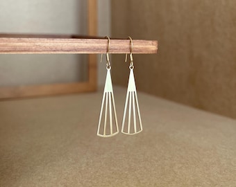 以下が含まれることがあります： 幾何学的な扇形のデザインの金色のイヤリングのペア。イヤリングは木製の表面にぶら下がっています。