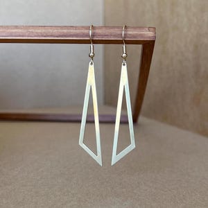 May include: A pair of gold-toned geometric earrings with a triangle shape. The earrings are long and dangle.