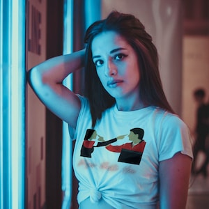 Puede incluir: Una camiseta blanca con un gráfico de dos personas que se señalan entre sí. El texto "We're not friends" está impreso debajo del gráfico.