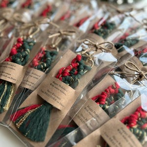 May include: A collection of small, red and green tassel keychains with gold accents. Each keychain is individually packaged in a clear plastic bag with a brown card attached. The card has a festive message that reads "Happy Holidays! With warm wishes, Slava Kleyman Your REALTOR on Duty".