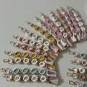 Puede incluir: Una colección de llaveros hechos a mano de colores con un diseño floral. Los llaveros están hechos con una variedad de colores, incluyendo rosa, amarillo, verde y blanco. Cada llavero tiene un anillo de metal dorado y una borla.
