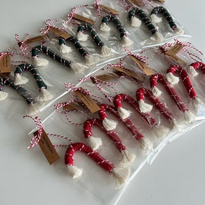 Könnte beinhalten: Eine Sammlung handgemachter Zuckerstangen-Ornamente, einige sind rot und weiß, andere grün und weiß. Die Ornamente sind in durchsichtigen Plastiktüten verpackt mit einem braunen Etikett, auf dem "Frohe Weihnachten" steht.