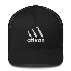 Puede incluir: Gorra de camionero negra con parte trasera de malla y visera curva. La gorra presenta la palabra "ativan" bordada en blanco, junto con un diseño estilizado de jeringa encima del texto. Estilo clásico de gorra de béisbol.