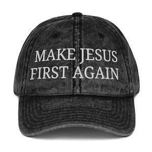 May include: A black baseball cap with the embroidered text "MAKE JESUS FIRST AGAIN" in white. The cap has a curved brim and a distressed, vintage look.