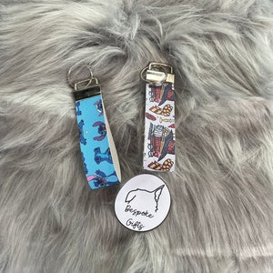 Könnte beinhalten: Zwei Schlüsselanhänger mit bunten Mustern. Der Schlüsselanhänger links hat einen blauen Hintergrund mit einem sich wiederholenden Muster von Stitch aus Lilo & Stitch. Der Schlüsselanhänger rechts hat einen weißen Hintergrund mit einem sich wiederholenden Muster eines Hogwarts Express-Zuges. Beide Schlüsselanhänger haben silberne Schlüsselringe.