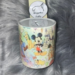 Puede incluir: Una alcancía de cerámica blanca con un diseño colorido que presenta a Mickey Mouse, Minnie Mouse, Donald Duck, Goofy y otros personajes de Disney. El diseño también incluye un castillo y globos. La alcancía tiene una ranura en la parte superior para monedas.