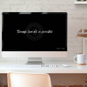 May include: A black computer screen with a white quote that reads "Through love all is possible" with a sunburst design. The computer is on a white desk with a white mug, a keyboard, and a mouse.
