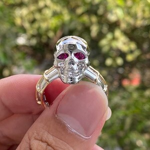 以下が含まれることがあります： ルビーの目と金のアクセントが付いたシルバーのスカルリング。スカルリングは、洗練された仕上げの、詳細なデザインが特徴です。リングのバンドは金色で、スカルの目は鮮やかな赤色です。