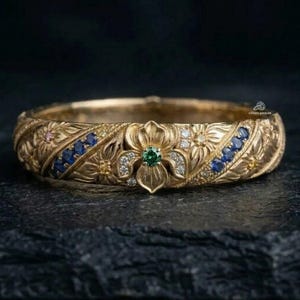 May include: A gold band ring featuring an intricate floral relief pattern. The center flower is set with a green gemstone, surrounded by small white diamonds. Two diagonal rows of blue sapphires and small yellow stones accent the floral design.