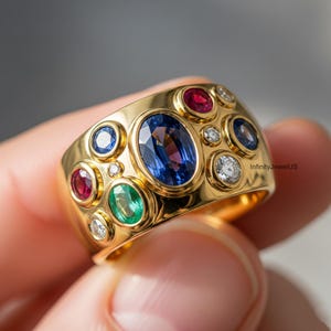 May include: A wide gold ring set with various gemstones. The ring features an oval blue sapphire, surrounded by smaller rubies, emeralds, sapphires, and diamonds. The ring is held by a hand.