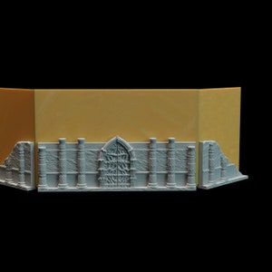 May include: A 3D printed model of a stone wall with a large arched doorway and columns. The wall is painted a light gray color and the background is a light yellow.