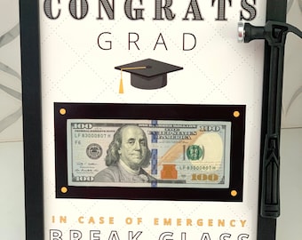 Peut inclure: Une image encadrée en noir avec un fond blanc et le texte "CONGRATS GRAD" en noir. Un bonnet de diplômé est au centre de l'image. Un billet de 100 € est derrière un rectangle noir avec le texte "EN CAS D'URGENCE CASSEZ LE VERRE" en dessous. Un petit marteau noir est sur le côté droit du cadre.