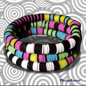 May include: Multi-colored beaded bracelet with black, white, pink, blue, and yellow beads. The bracelet is made of multiple strands of beads and is layered.